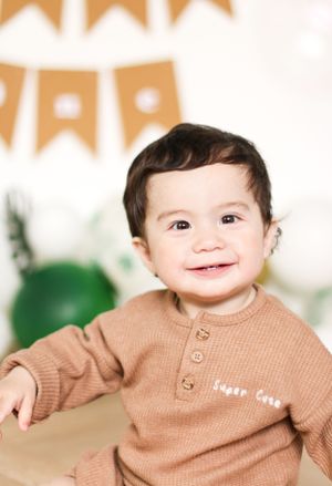 A smiling toddler in a tan sweater with decorative bunting in the background.