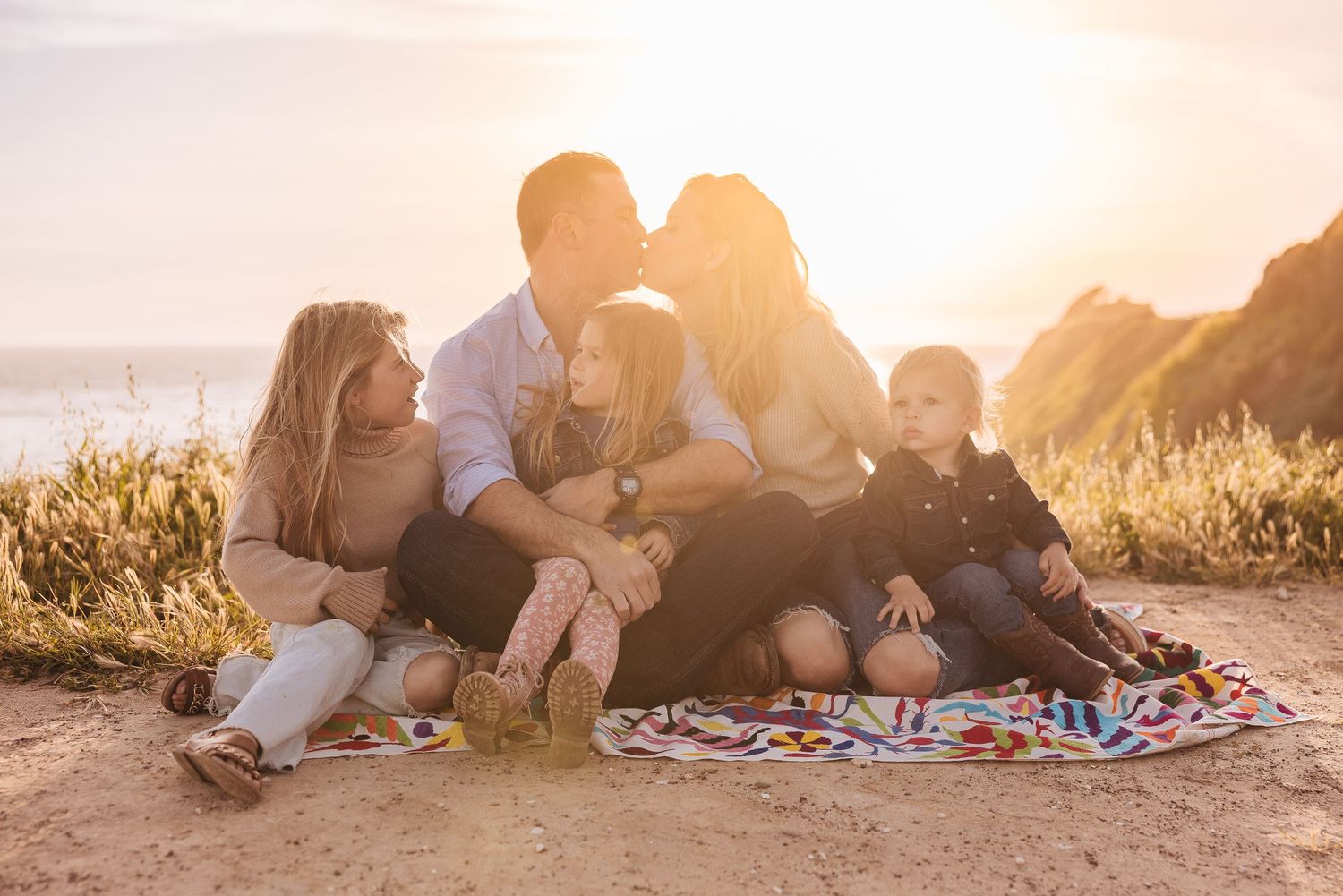 Family sitting on blanket at a beach in Santa Barbara with golden sun set in the background.