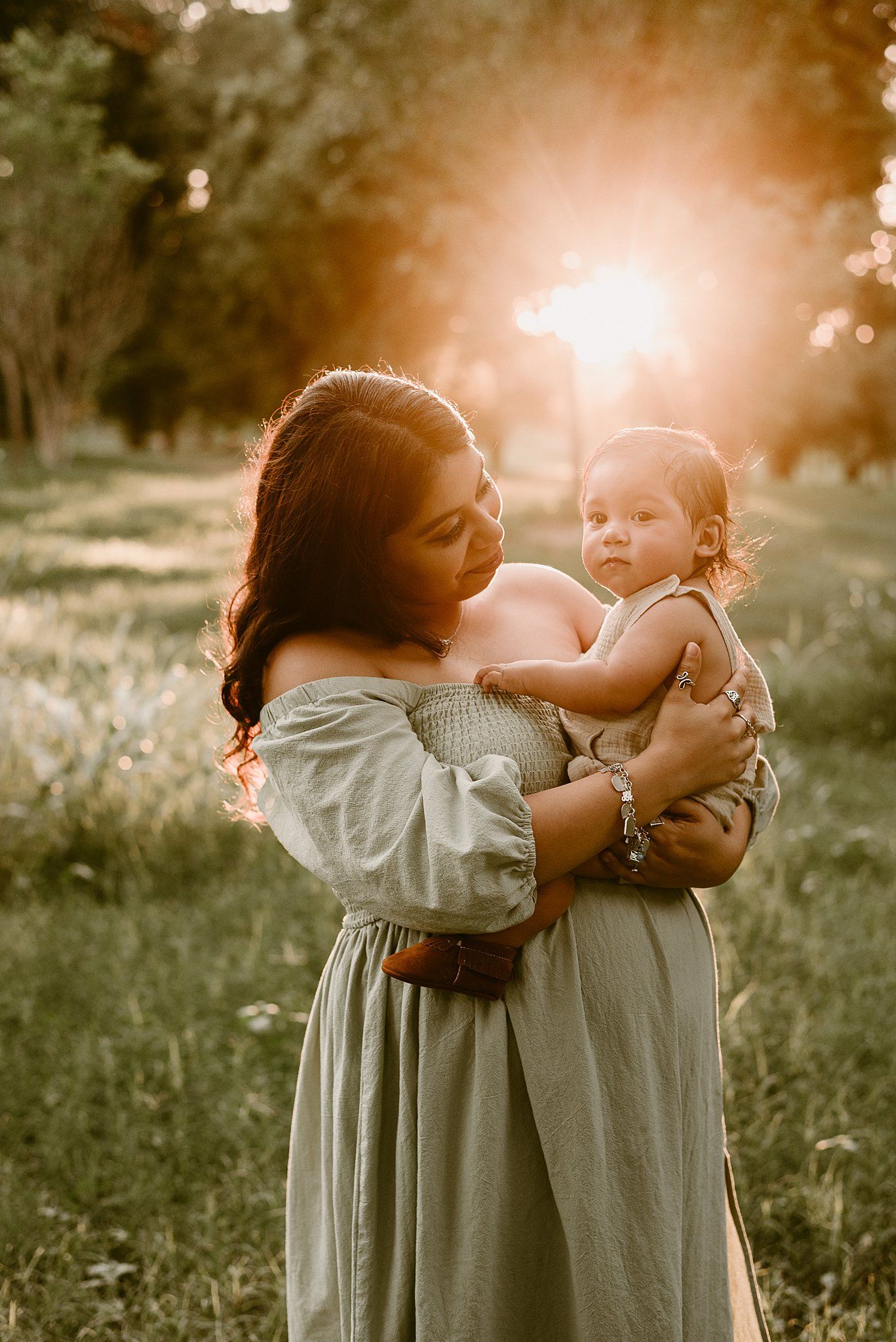 Backlit portrait of a woman holding a small child in a flowy dress during golden hour.
