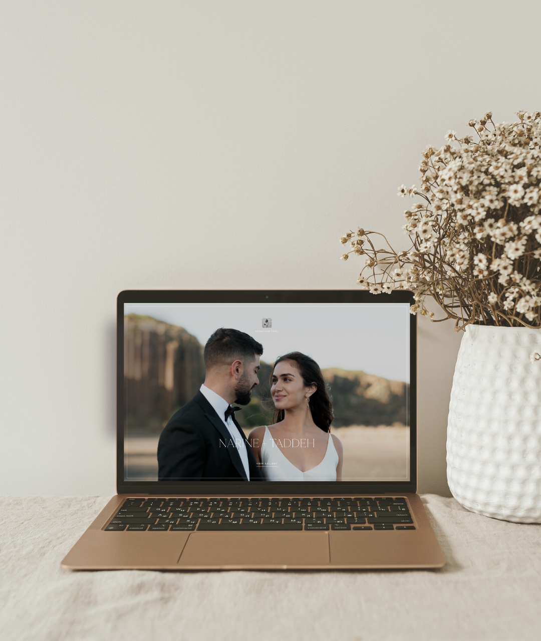 A wedding photo displayed on laptop screen with dried flowers in white vase.