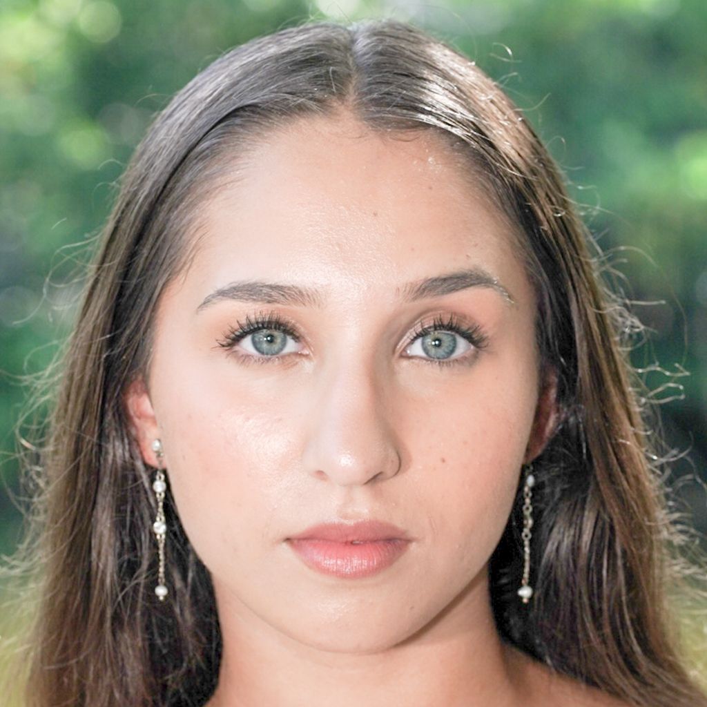 Close-up portrait of a young woman with striking blue eyes and dangling earrings against a blurred green background.