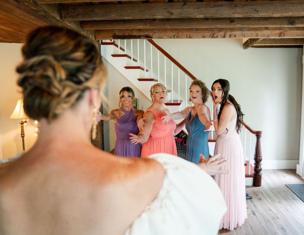 Bridesmaids in colorful pastel dresses share a candid moment on a staircase during wedding preparations.