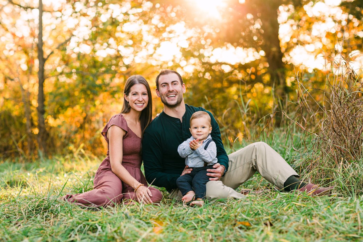 Family sits together on grassy hill during golden hour autumn photoshoot.