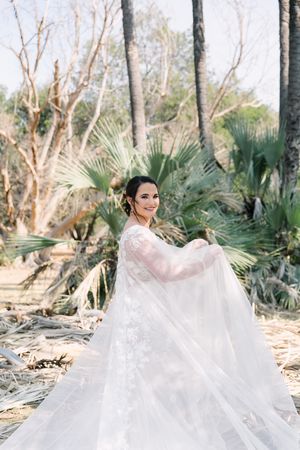 Johane standing amongst lala palms while lifting her custom made couture Casper Bosman bridal cape and dress.