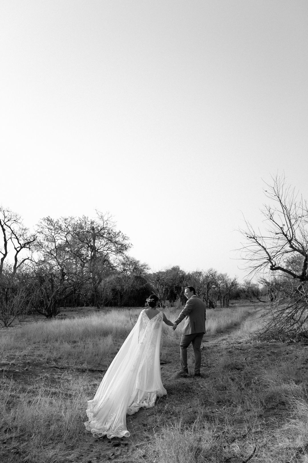 A groom leading his bride by the hand while walking away in the sunset.