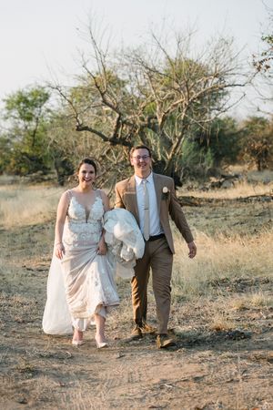 A laughing wedding couple walks towards to camera on their bushveld wedding day.