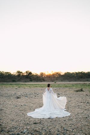 An expansive view of the bushveld and a bride's wedding cape billowing in the wind at sunset.
