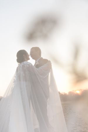 A hazy sunset with a wedding couple hugging close.