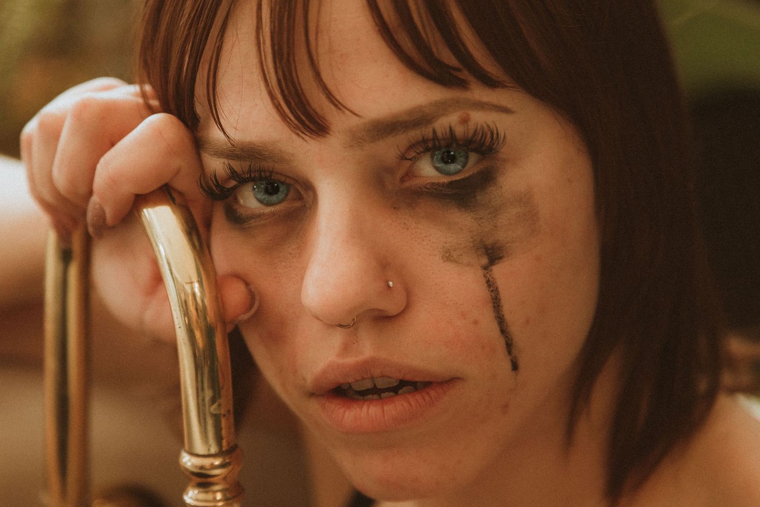 Moody close-up portrait featuring dark smudged makeup and a gold-colored prop.