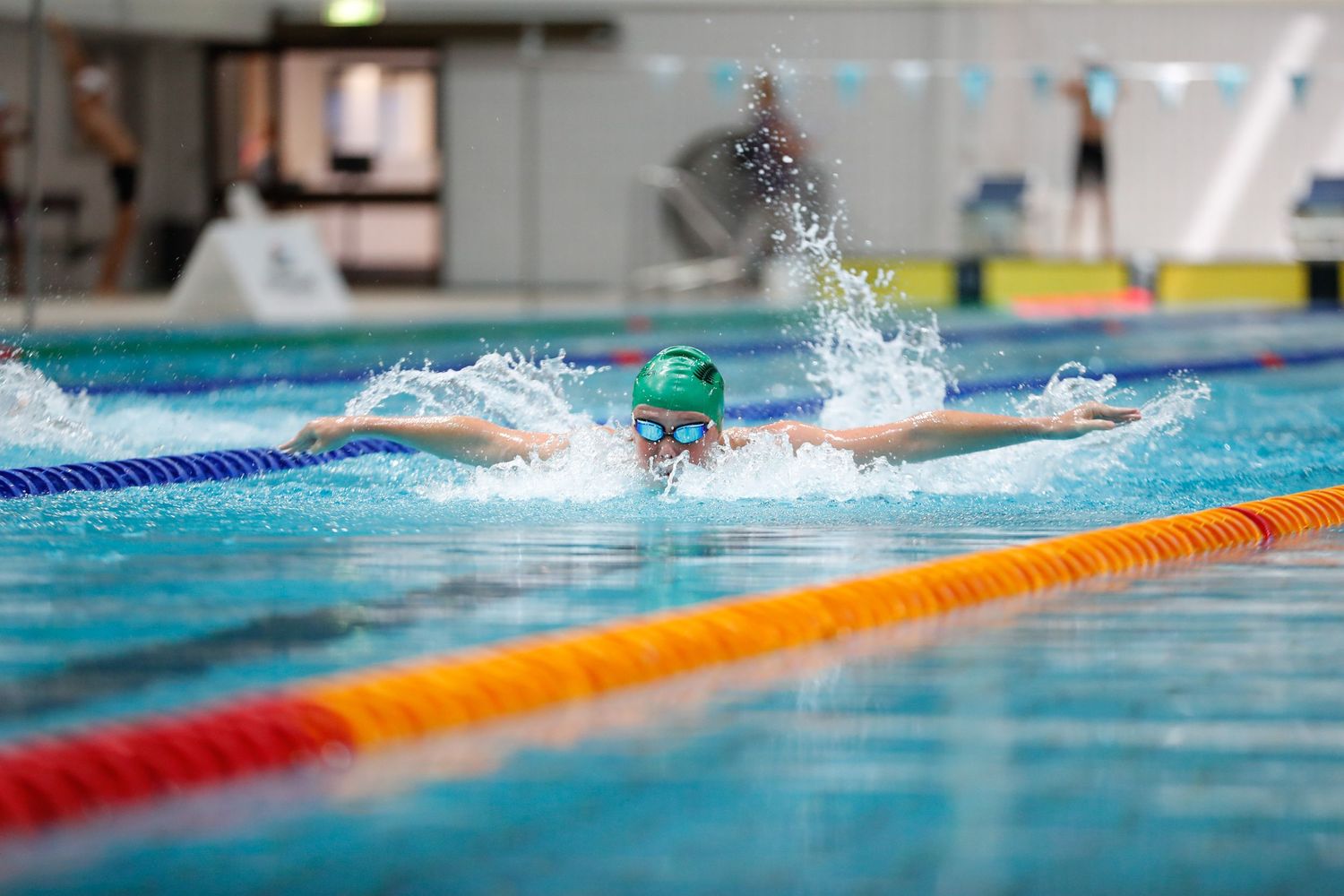 Competitive swimmer creating splash while racing in pool with orange lane markers.