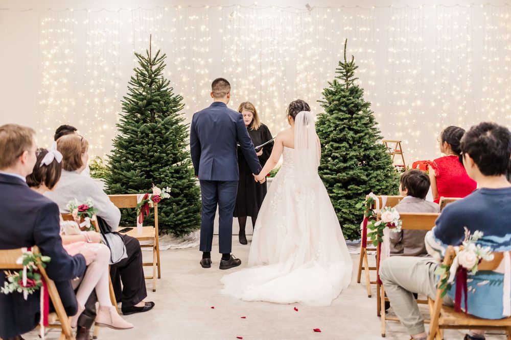 Bride and groom exchange vows at indoor winter wedding ceremony with Christmas trees.