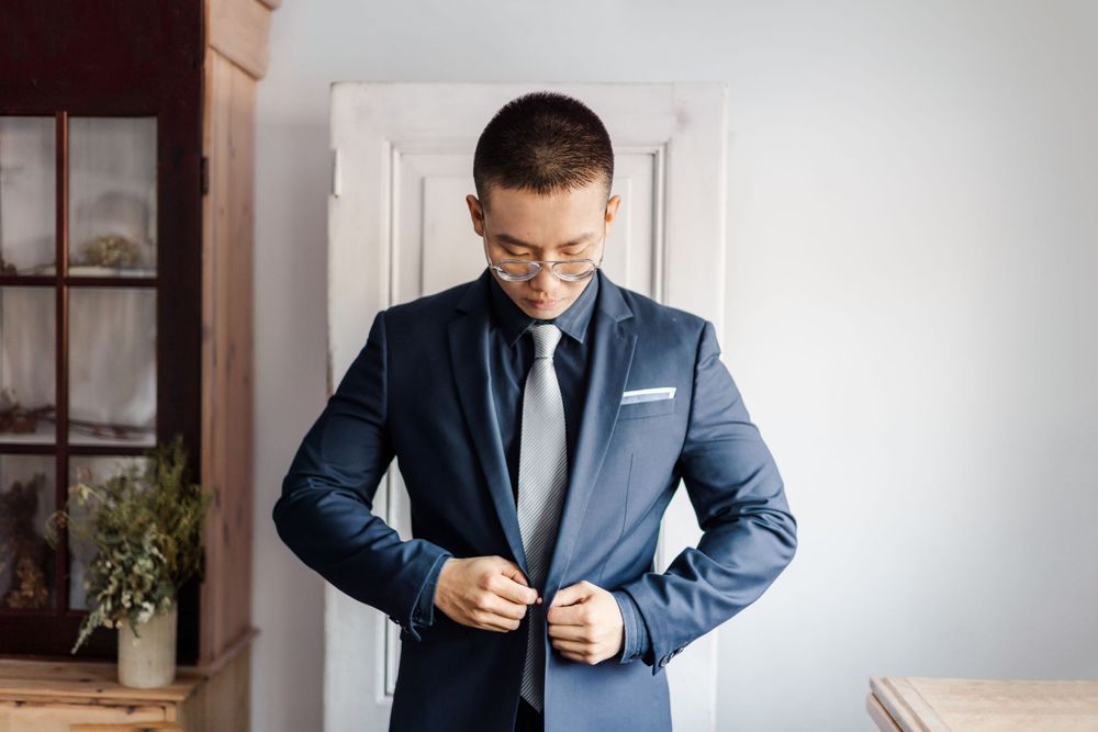 Groom in navy suit and tie buttons his jacket while getting ready for wedding.