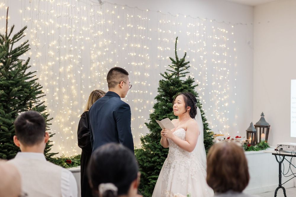 Bride and groom exchanging vows at indoor winter wedding ceremony with fairy lights and Christmas trees.