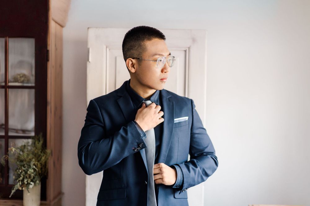Groom in navy suit adjusts his tie while preparing for the wedding ceremony.