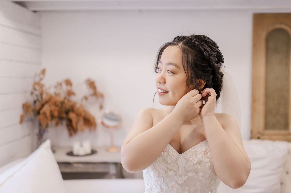 Bride in strapless lace gown puts on earrings while getting ready for wedding.