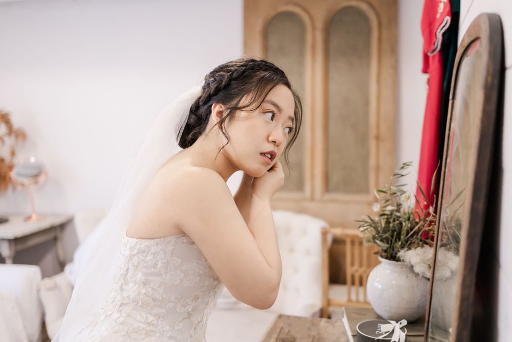 Bride in white lace dress examines herself in mirror during wedding preparation.
