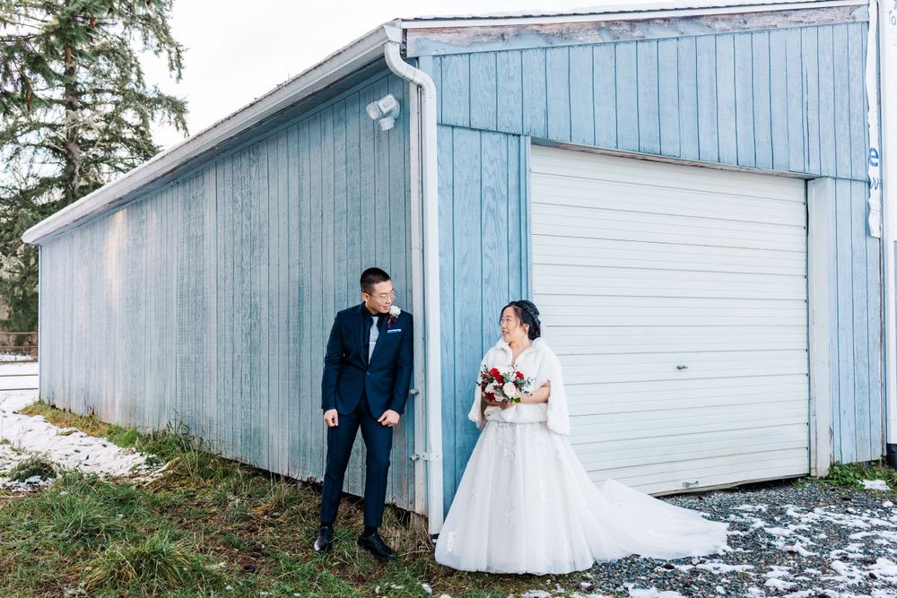 Bride and groom share a romantic first look beside a rustic blue barn in winter.