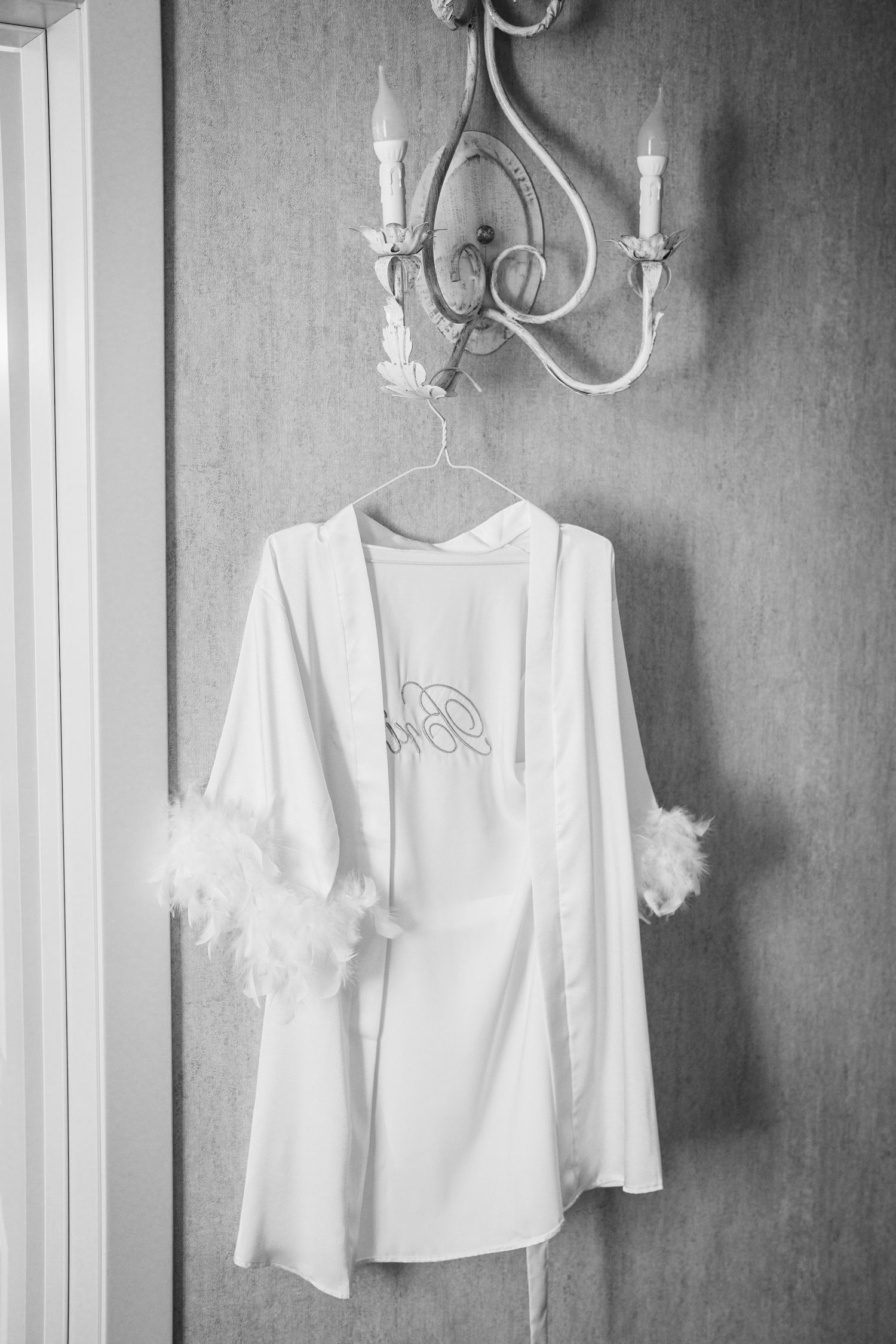 White silk robe with feather trim hanging under an elegant chandelier.