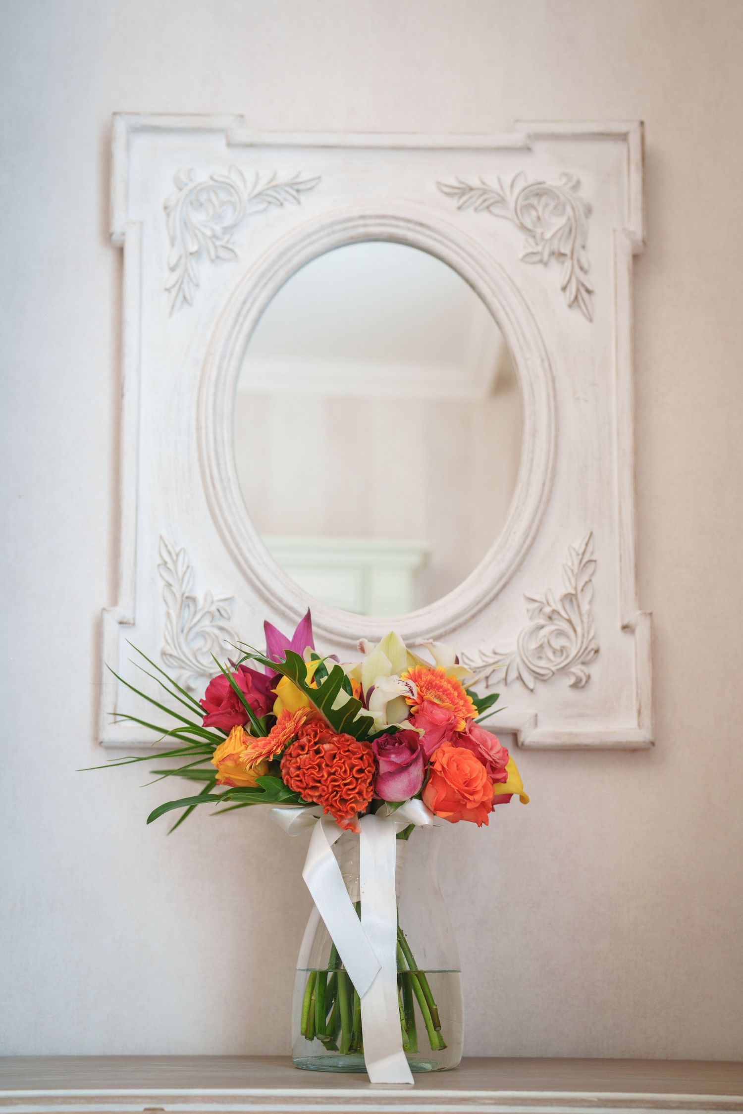 Vintage white oval mirror frame with colorful floral bouquet in vase below.