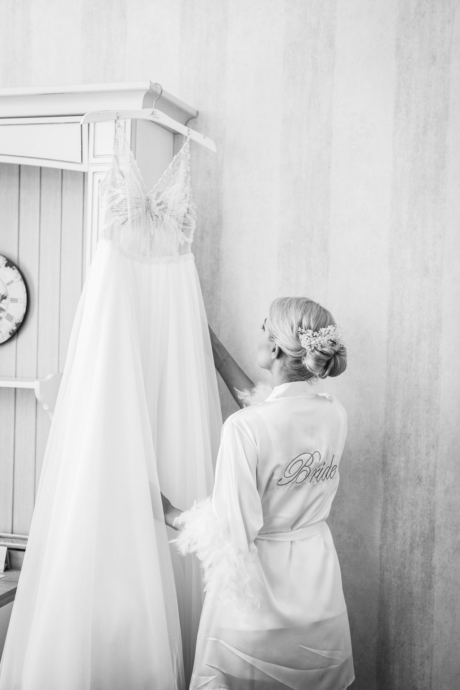 A white wedding dress hangs while someone in a silk robe looks on.