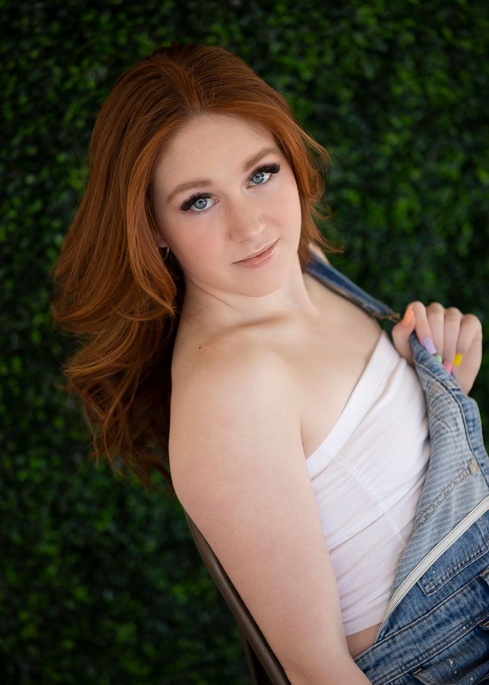 Stylish portrait against green hedge wall with white top and denim jacket.