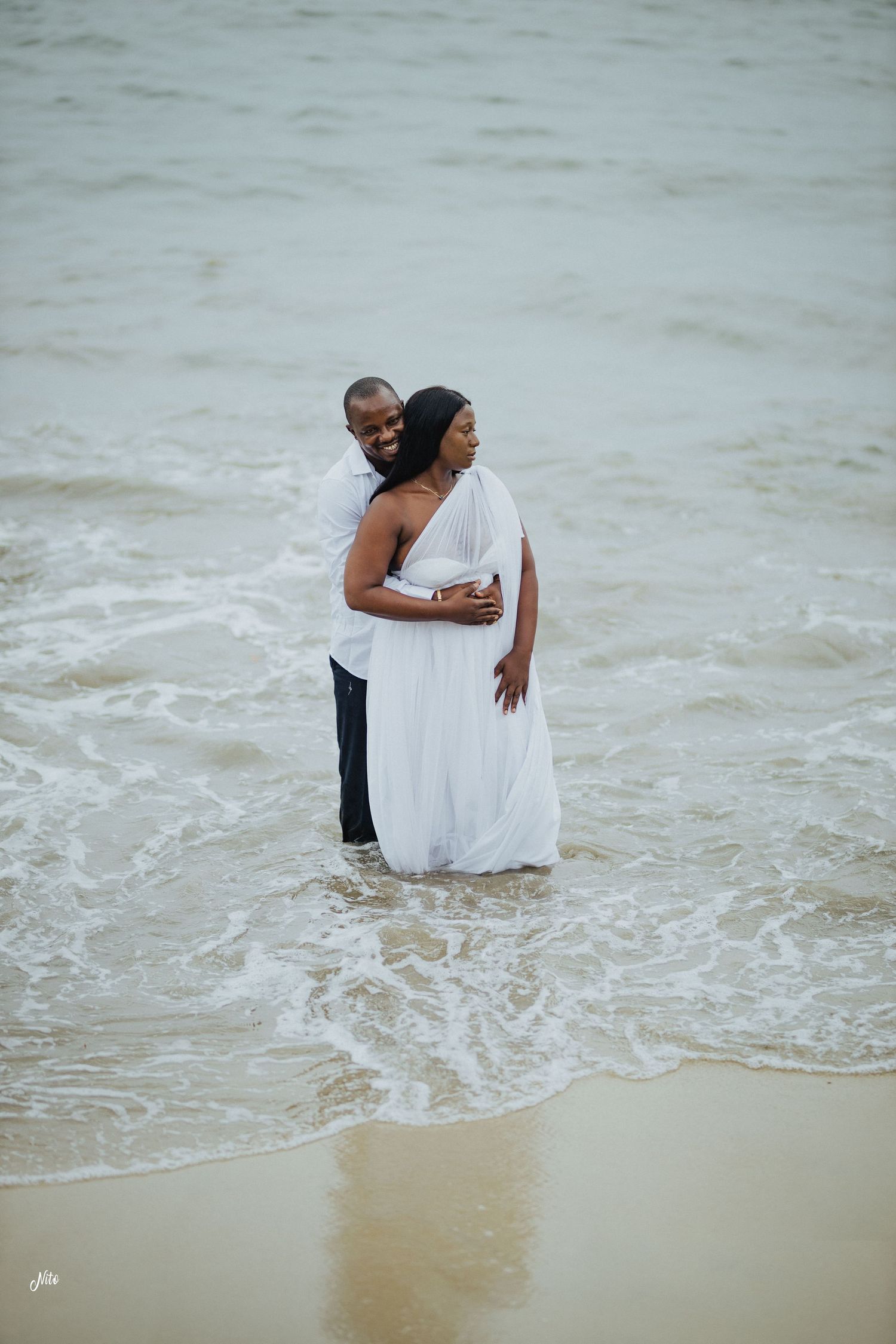 Couple embracing in the ocean waves during their beach photoshoot.