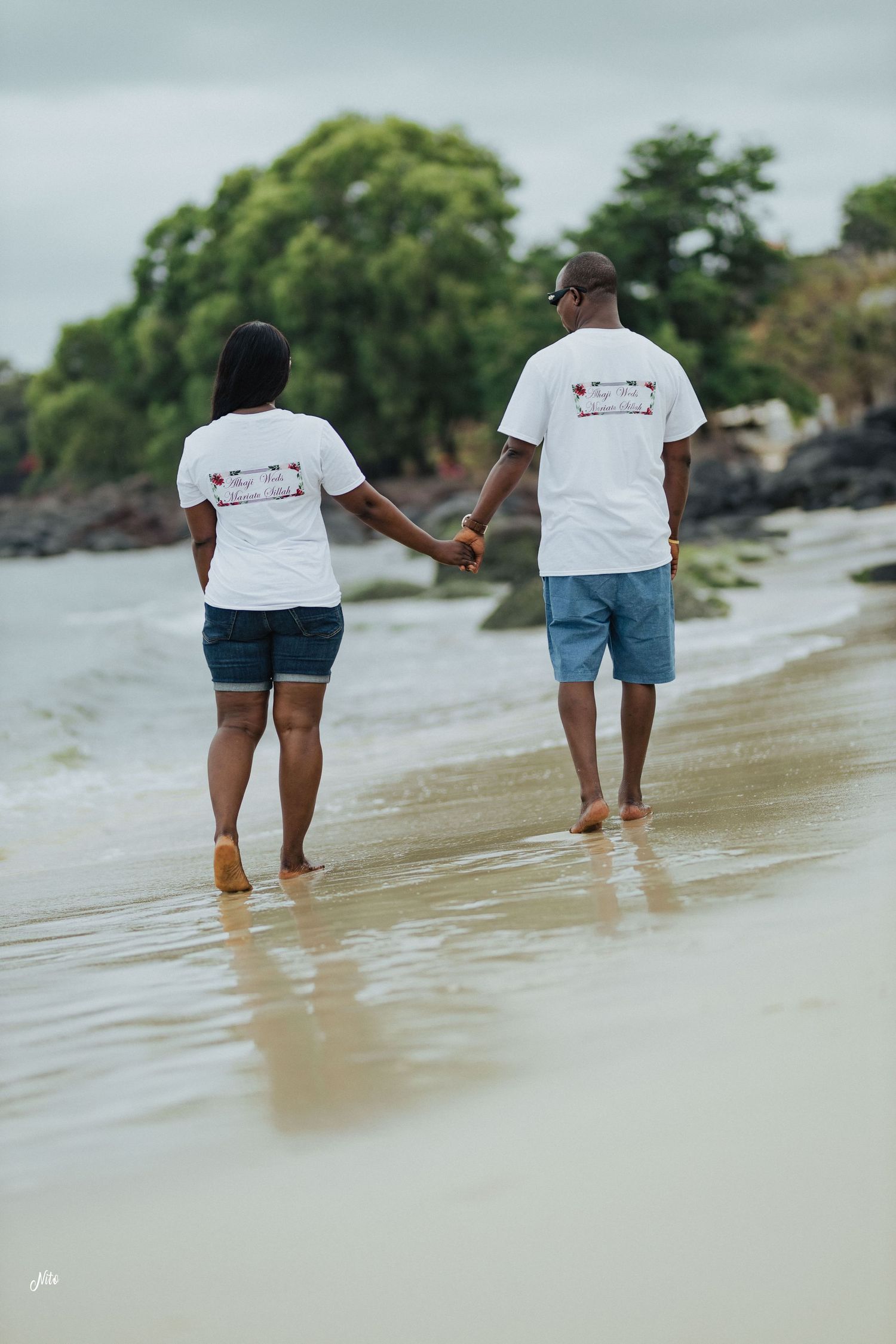 Couple in matching white t-shirts walking hand in hand on a beach.