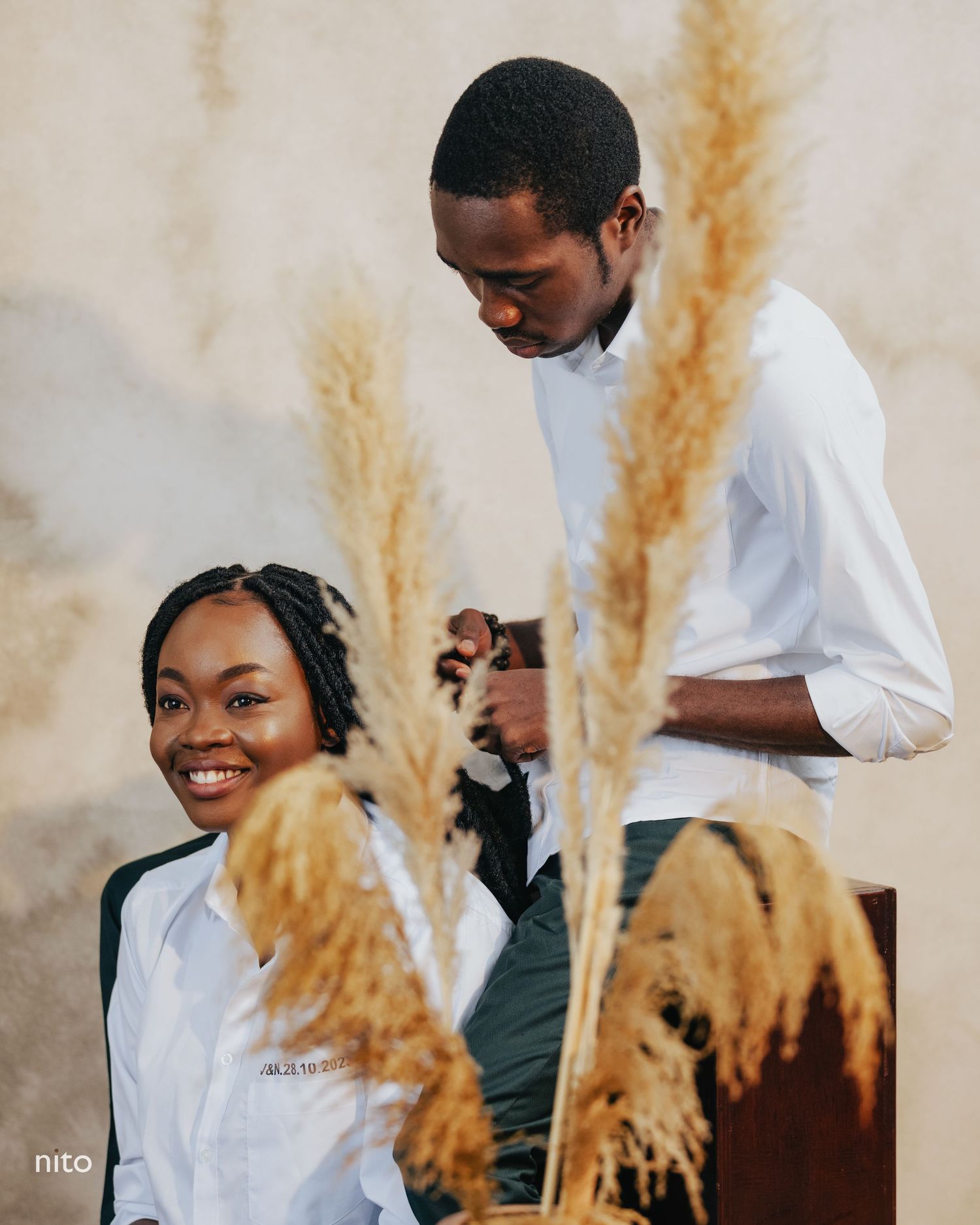 Couple in white shirts photographed with decorative pampas grass creating a romantic atmosphere.