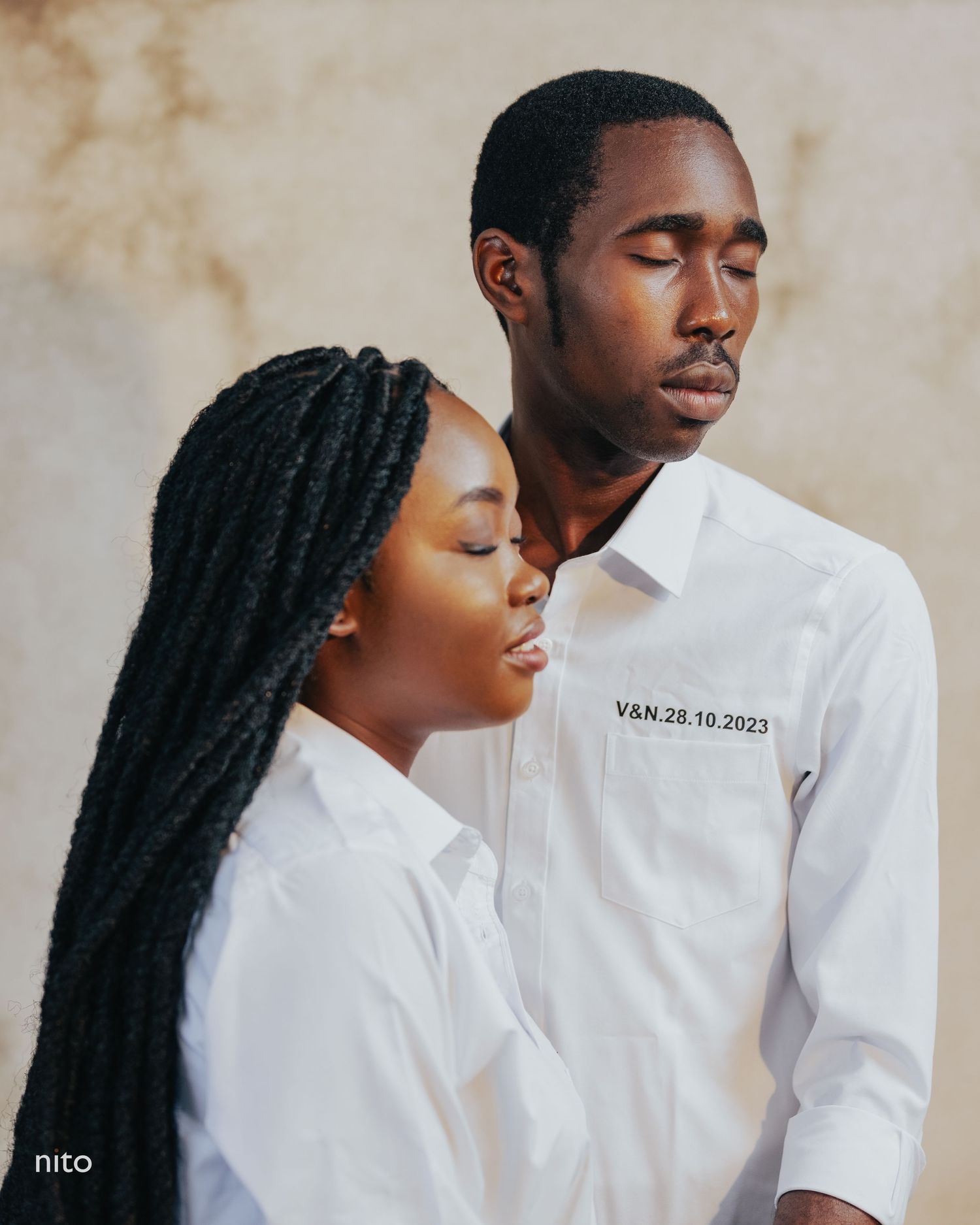 Intimate portrait of a couple in white shirts posed closely together against a neutral wall.