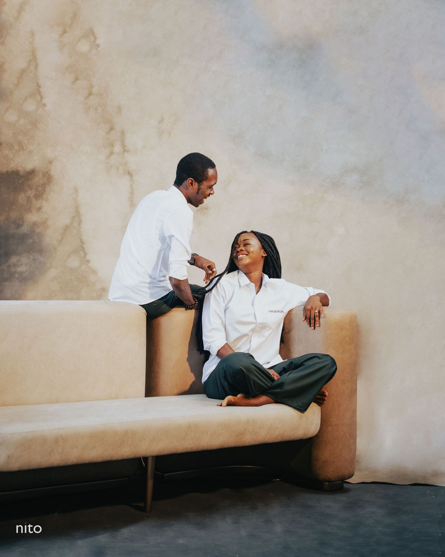 Couple sharing a candid moment on a beige couch in an artistic photoshoot.