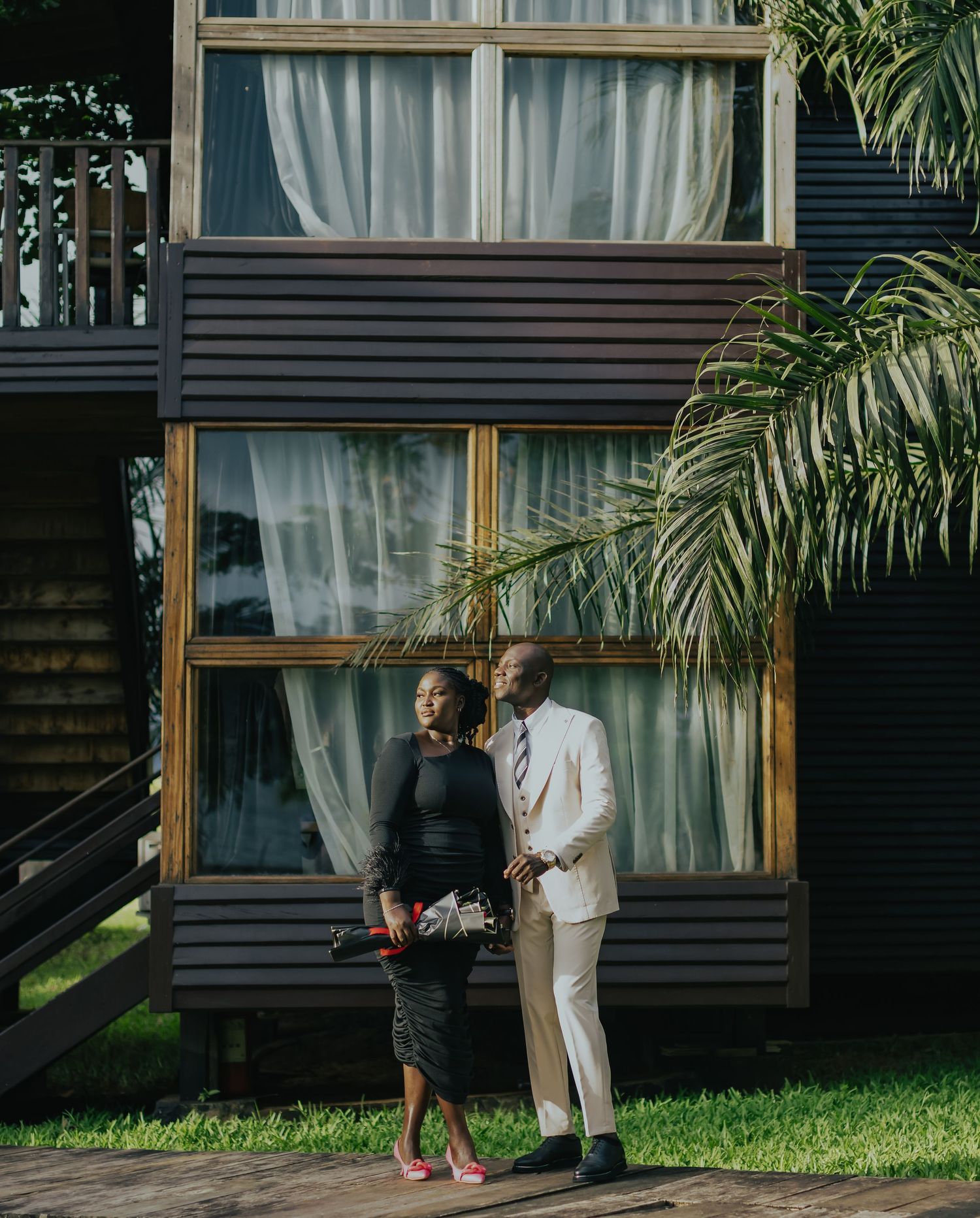 Well-dressed couple standing together against modern architectural backdrop with palm trees.