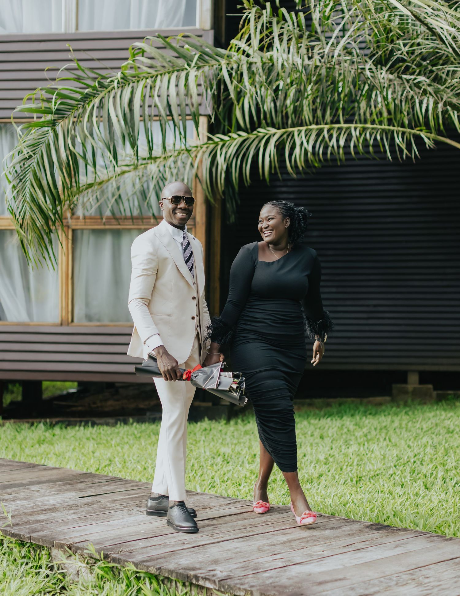Elegant couple walking outdoors, wearing contrasting black and white formal outfits near a modern building.