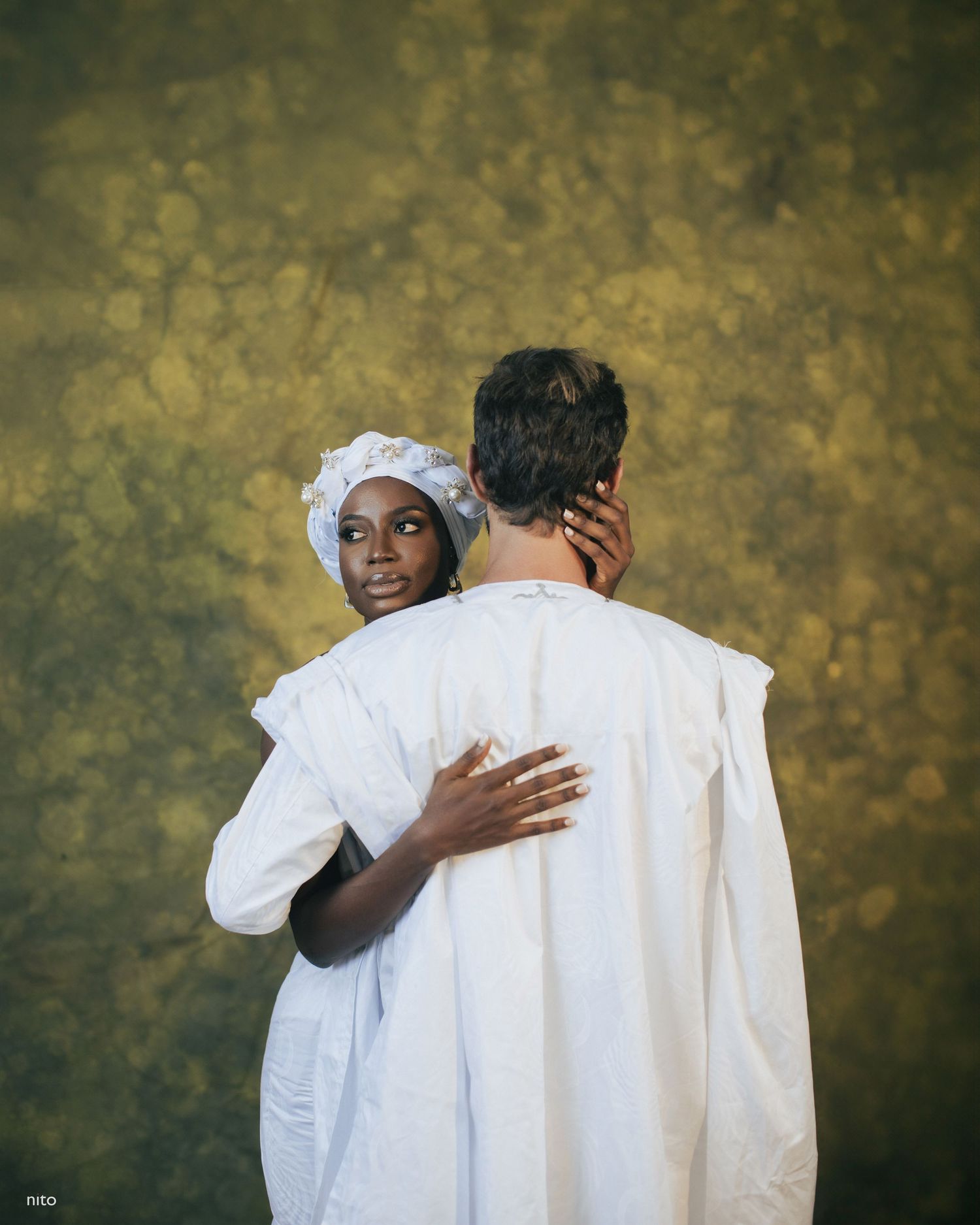 Intimate wedding portrait showing couple embracing in white attire against golden background.