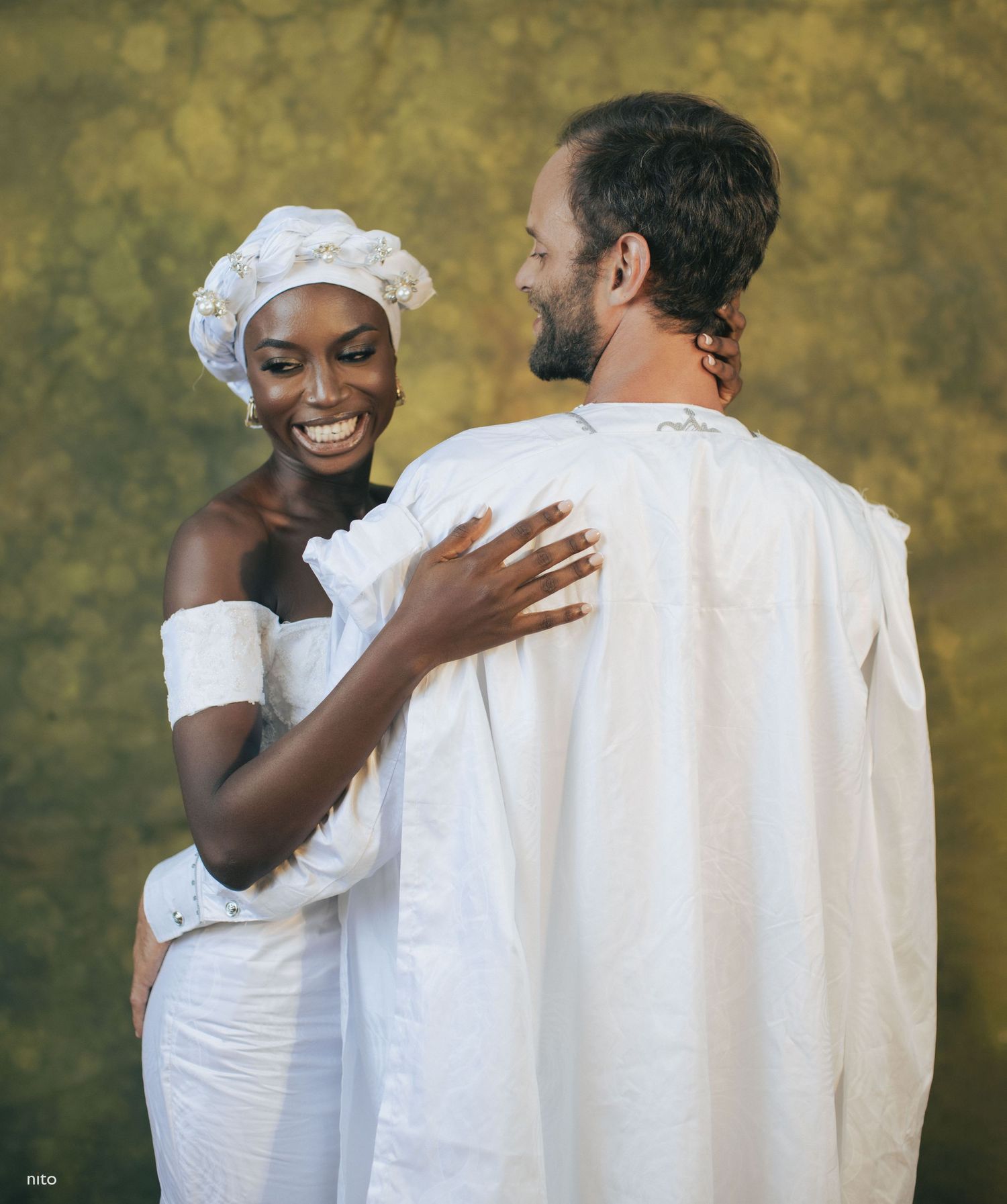 Joyful wedding moment captured as couple shares embrace against textured backdrop.