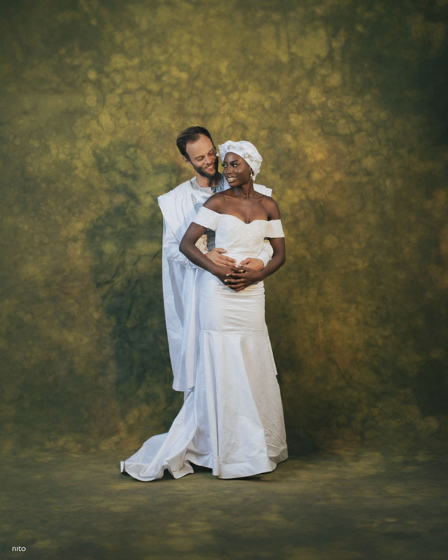 Romantic wedding portrait showing couple in white embracing against golden backdrop.