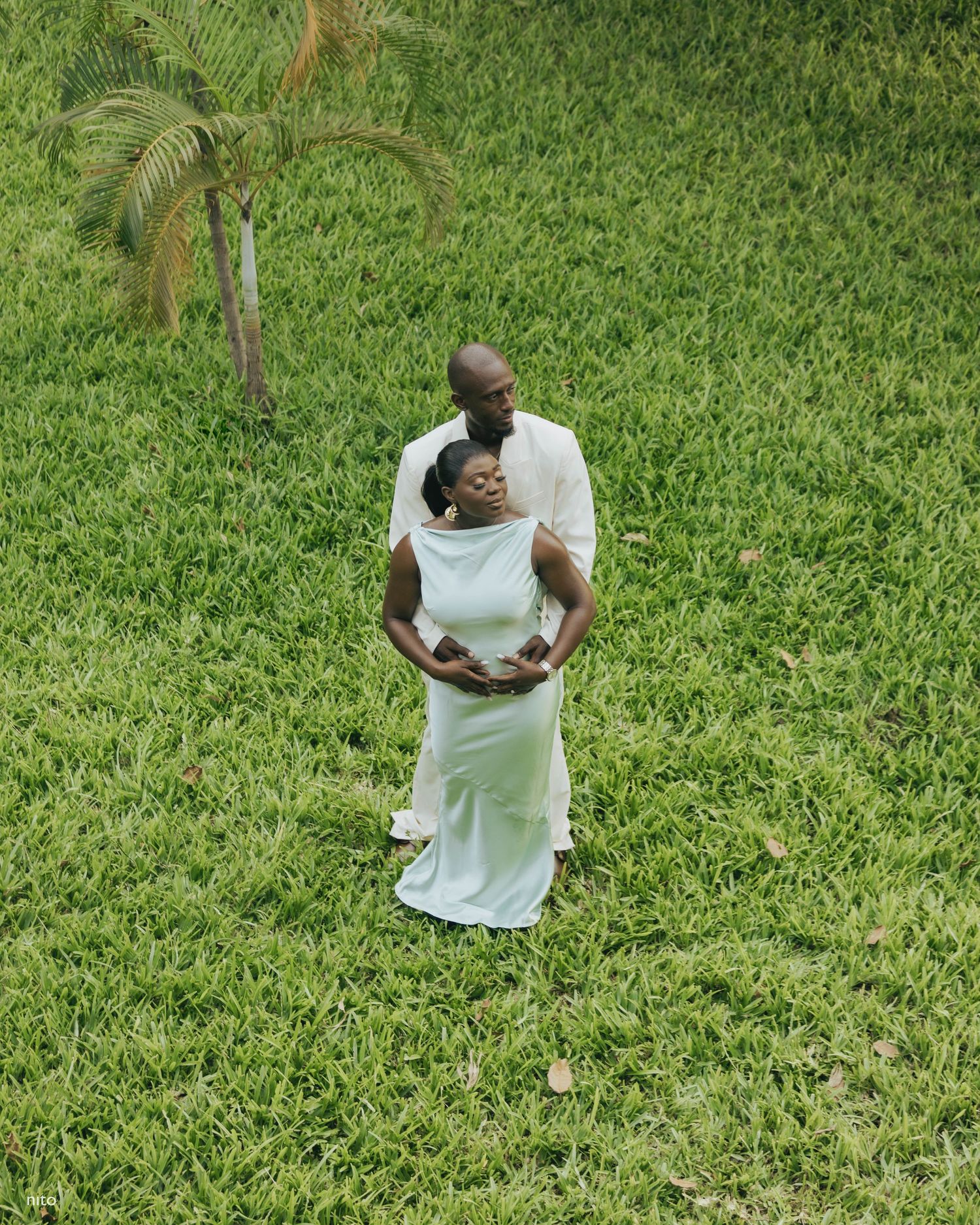 A couple shares a romantic moment while standing in a lush green garden setting.