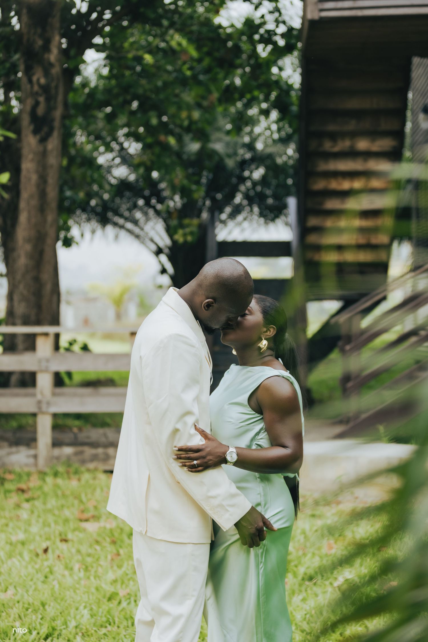 A couple shares a tender embrace outdoors with rustic wooden fencing in the background.
