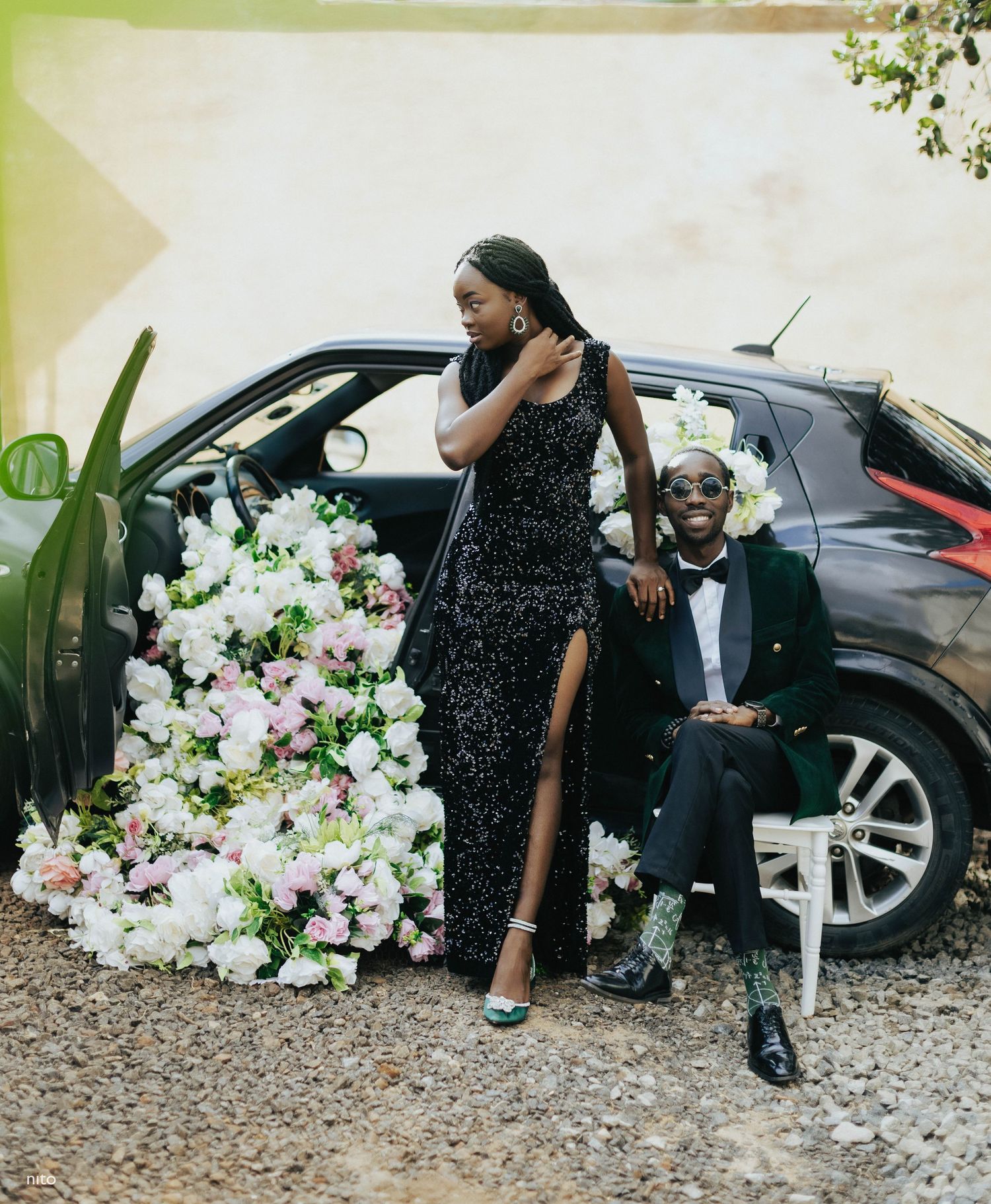 Formal couple posing by car decorated with white and pink flowers.