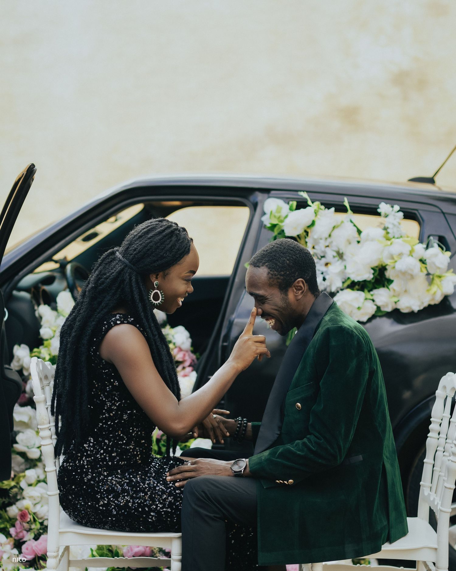 Sweet moment shared between couple by car door surrounded by white floral arrangements.