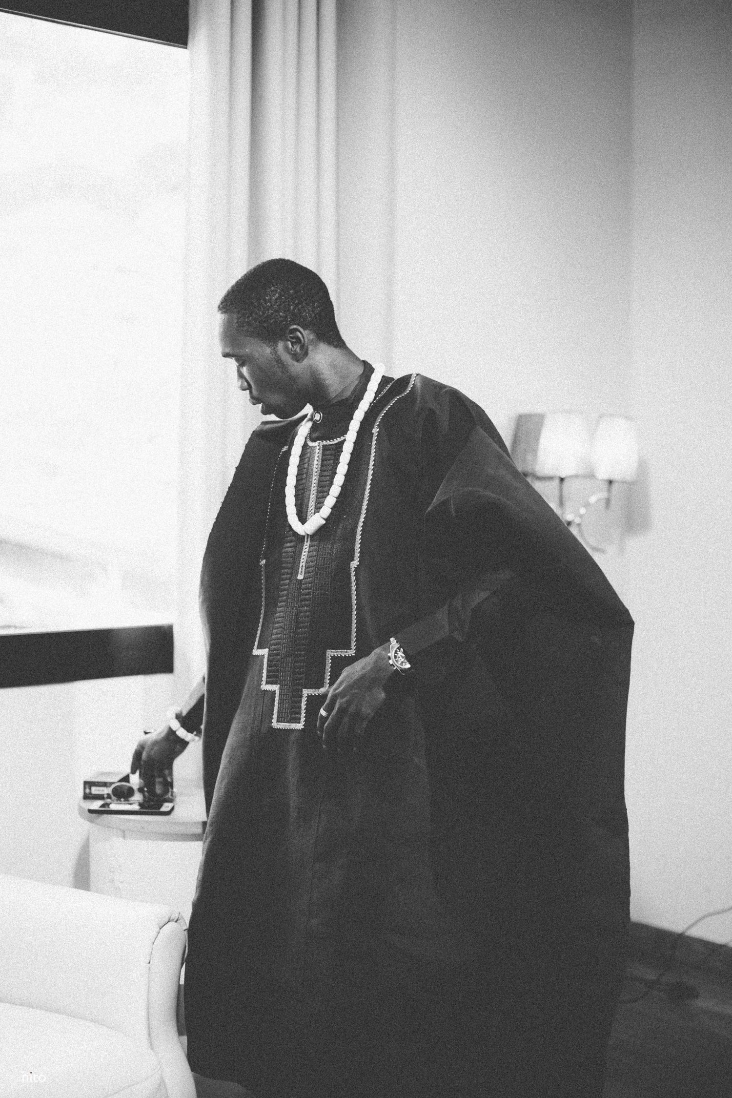 Black and white portrait of someone wearing a traditional black agbada with white beaded necklace.