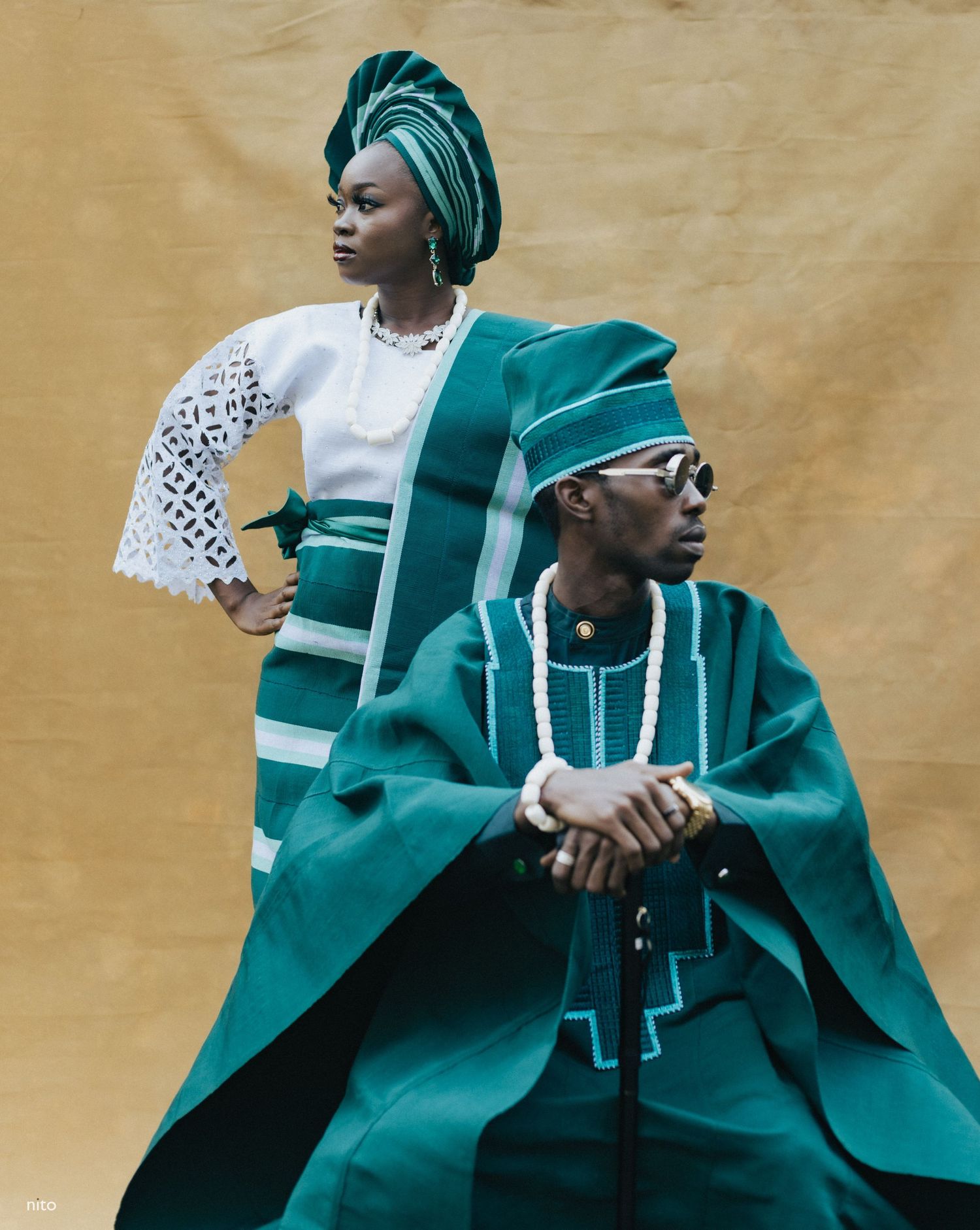 Traditional couple in emerald green and white Nigerian wedding attire against gold backdrop.