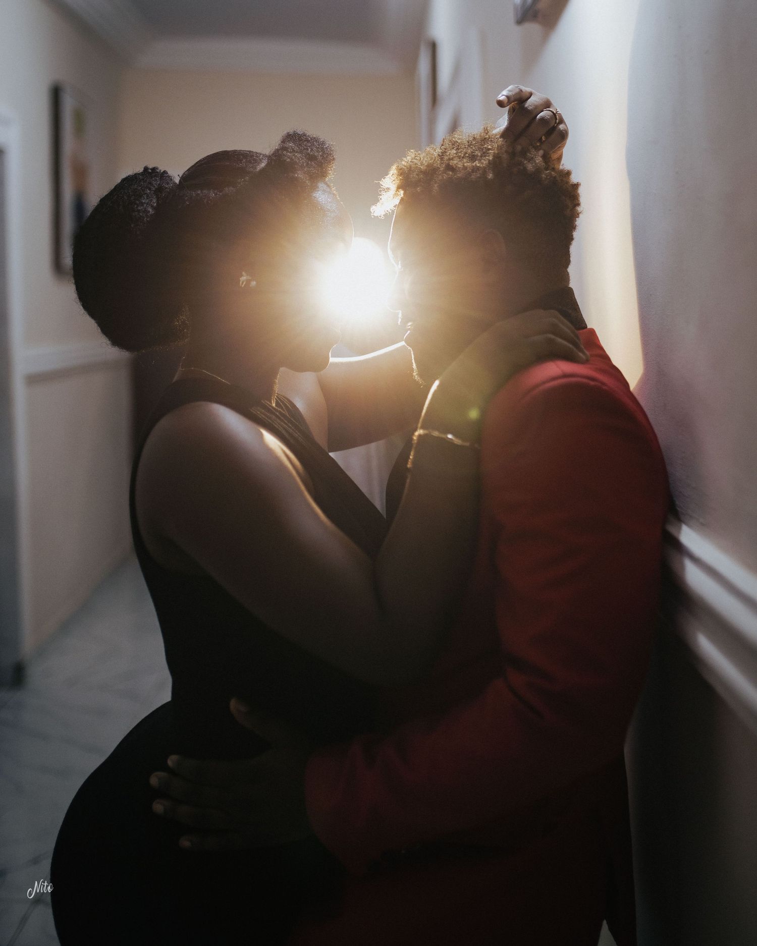 An intimate silhouetted moment between two people in a sunlit hallway.