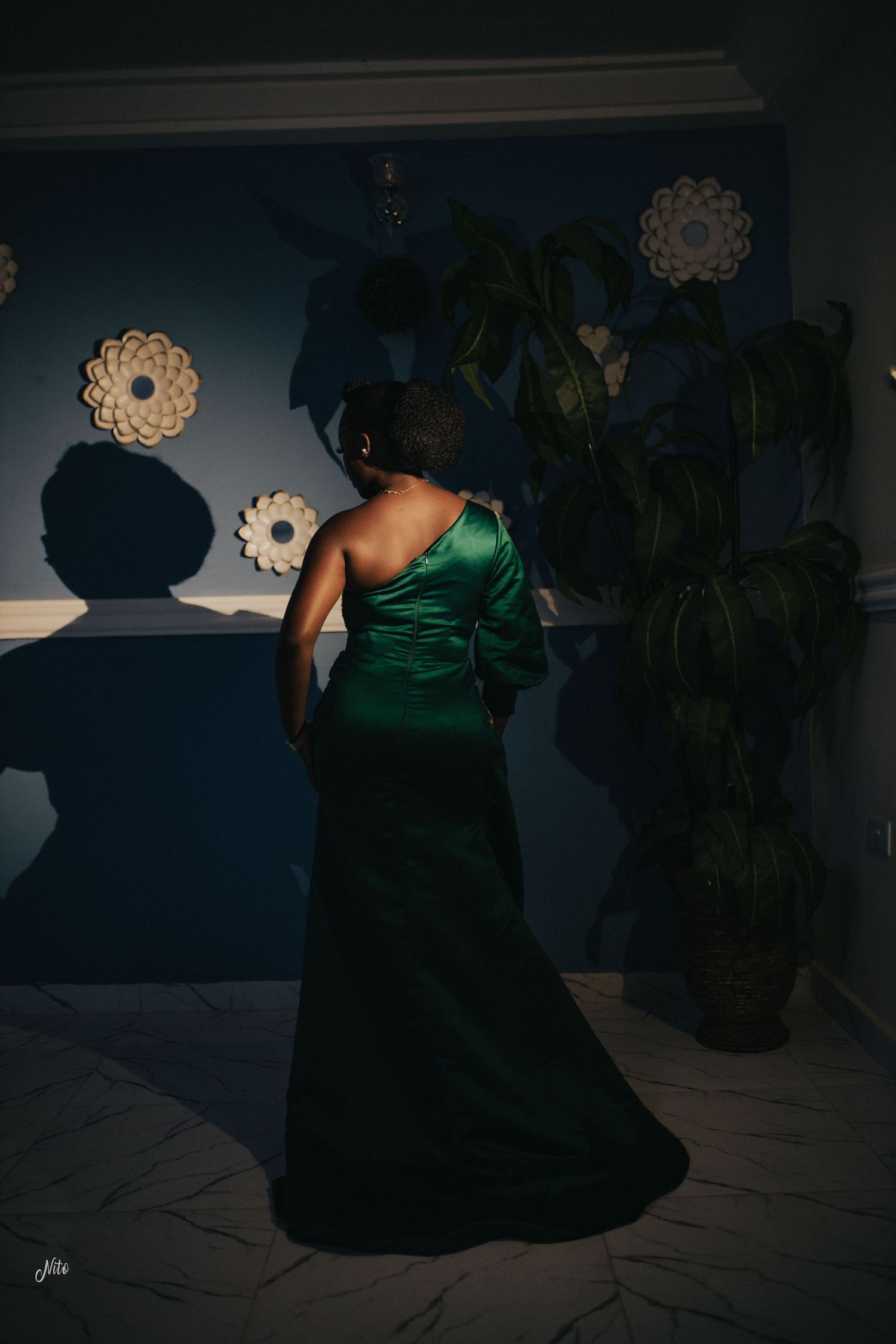 A person in an elegant emerald green evening gown poses dramatically in moody lighting.