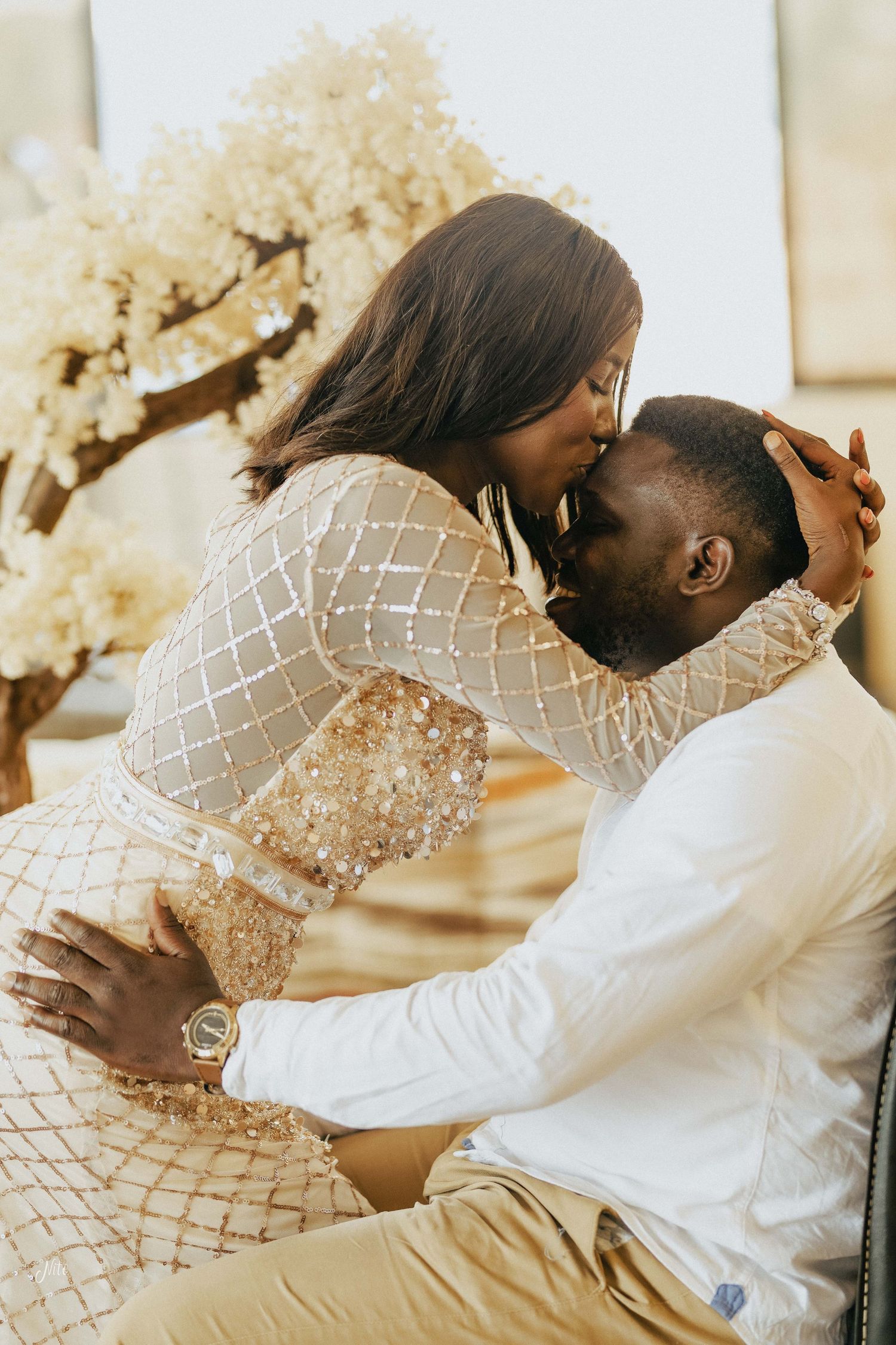 A romantic embrace near a blooming tree with sunlight filtering through.