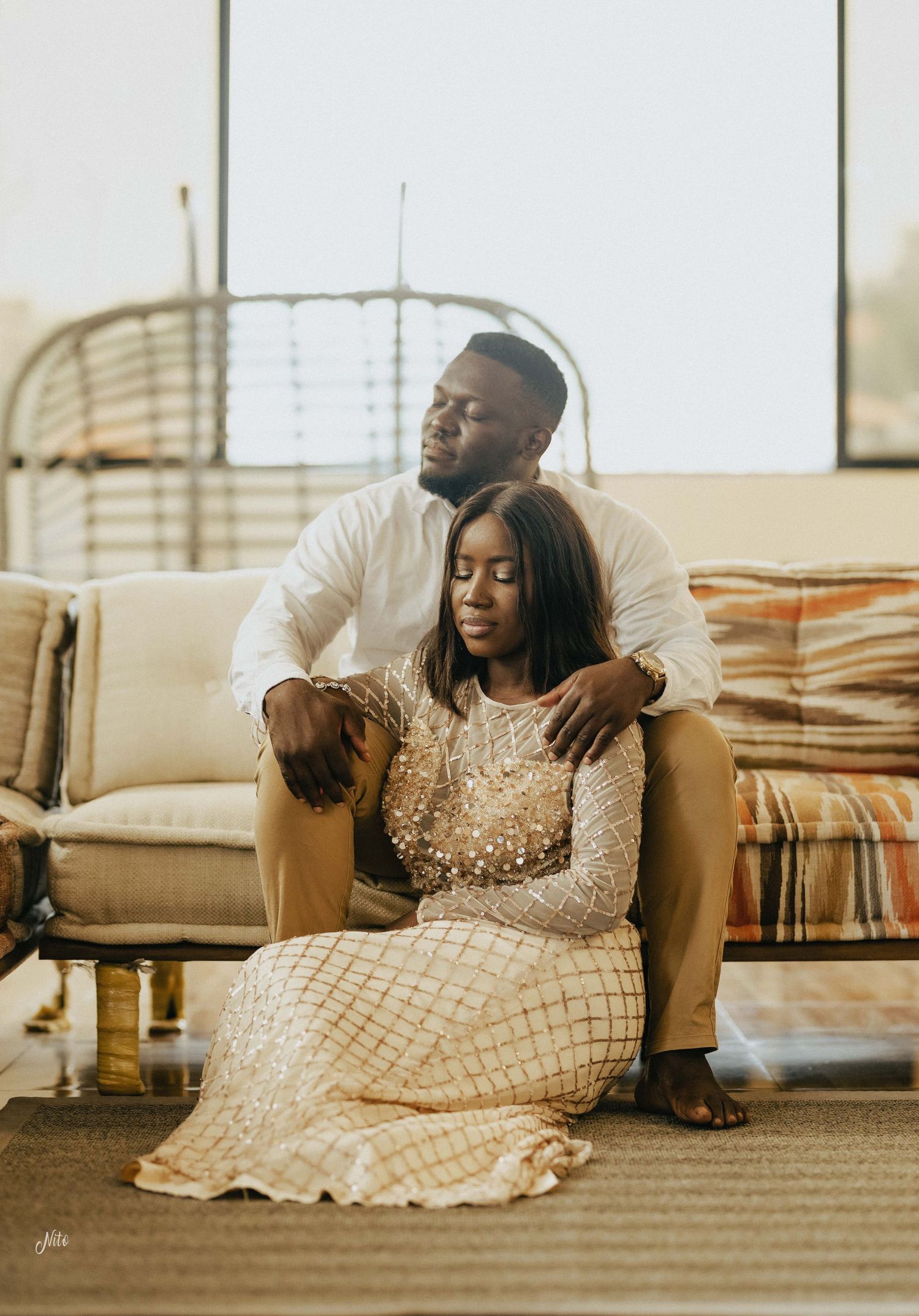 An intimate portrait of a couple in a sun-lit room with decorative furnishings.