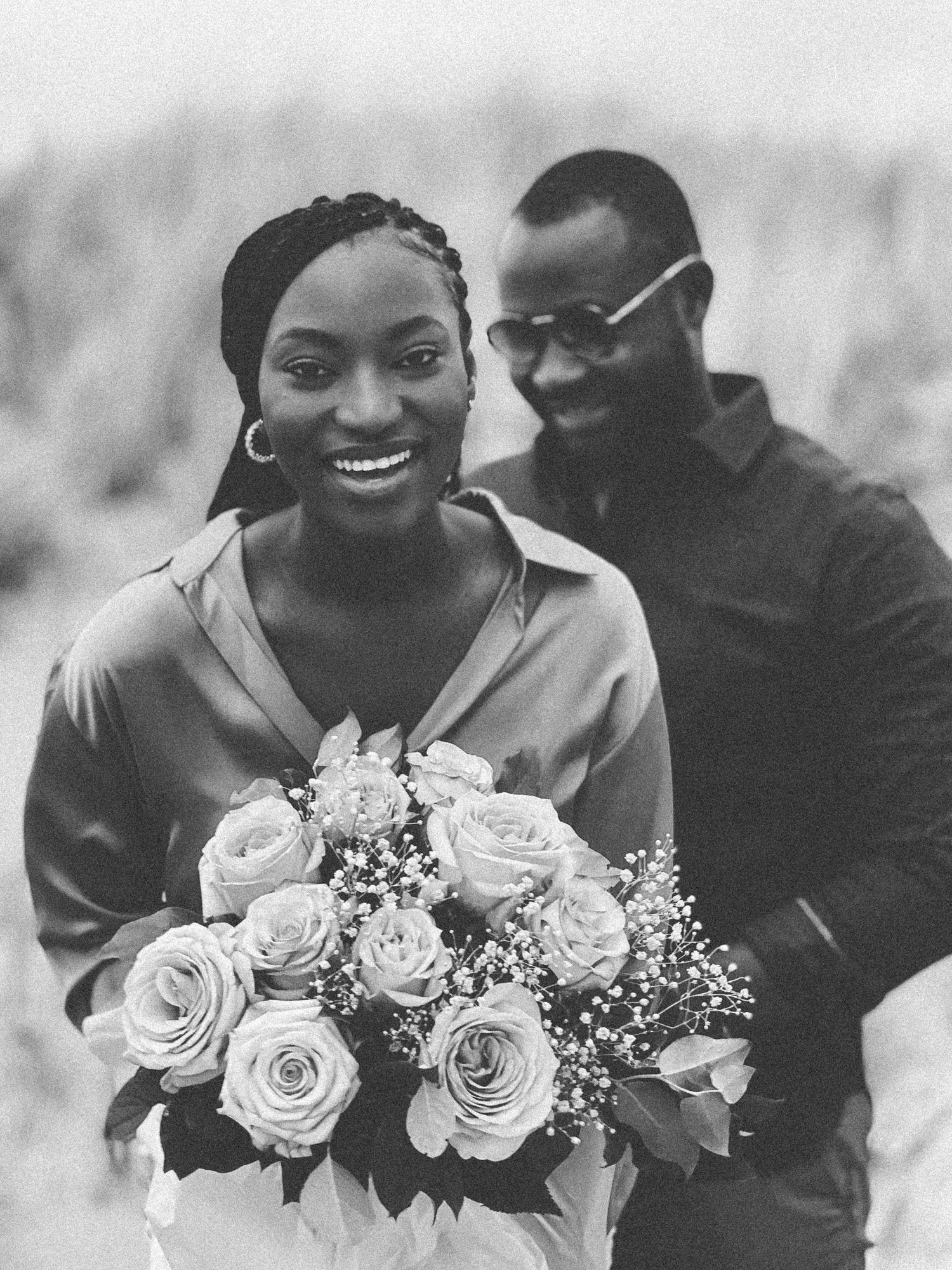 A happy couple sharing a tender moment with a beautiful bouquet of white roses in a black and white photo.