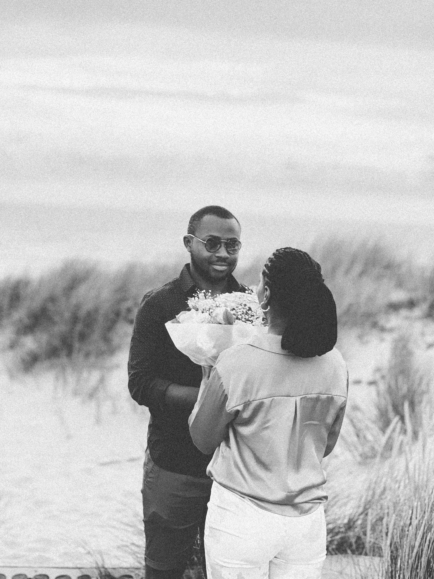 A couple exchanging flowers and smiles during an outdoor photoshoot in monochrome.