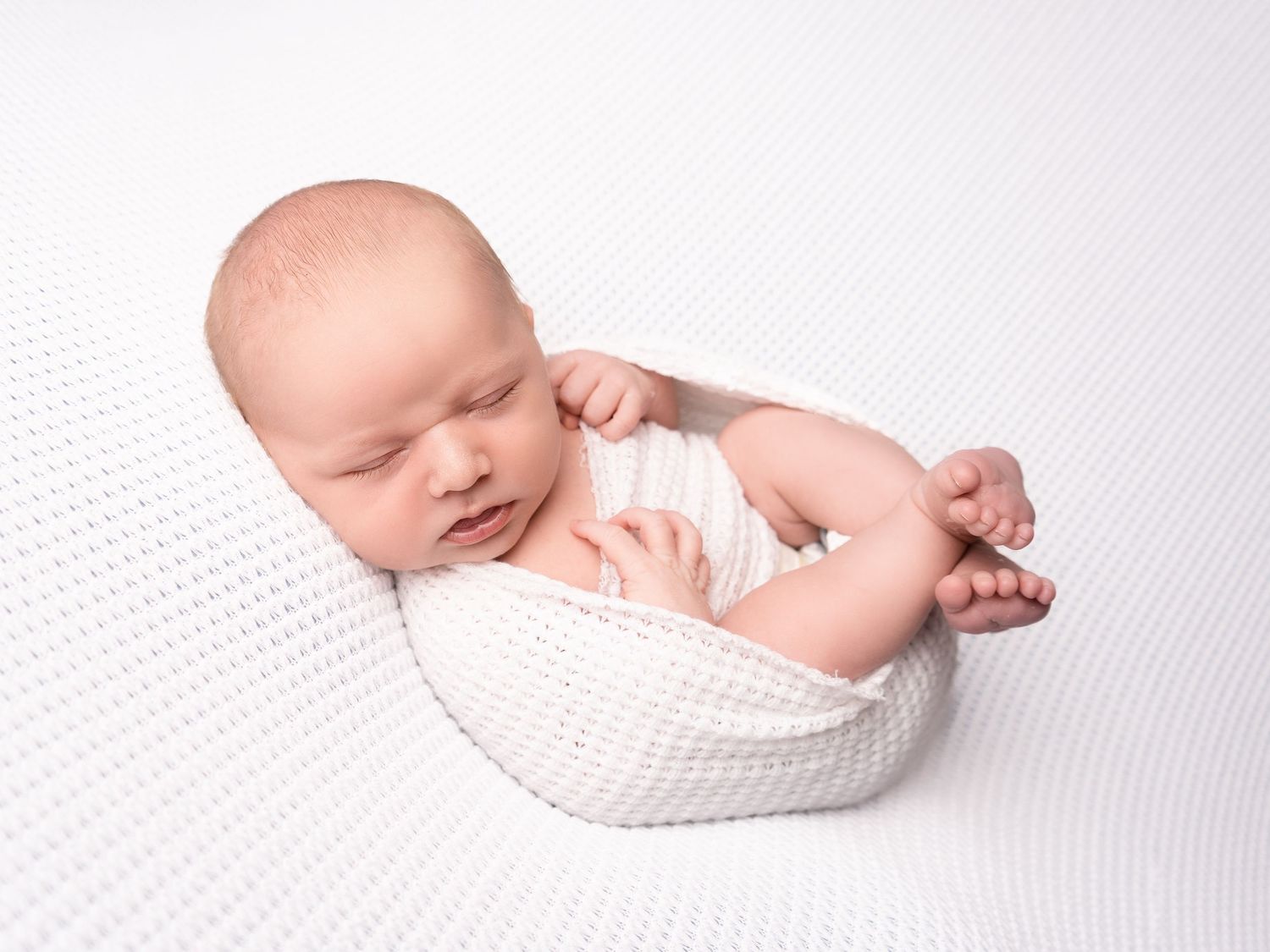 baby boy sleeping on a white cosy knitted blanket wrapped up with toes out at newborn photoshoot in Doncaster.