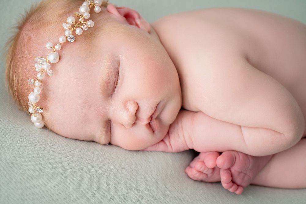 Peaceful sleeping newborn with pearl headpiece on mint green background.