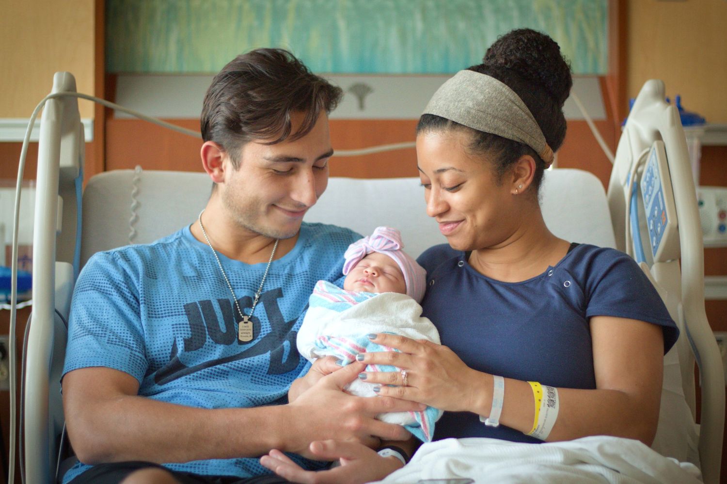 New parents admiring their swaddled newborn baby in a hospital room.